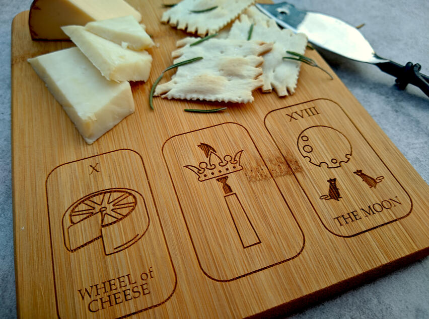 a bamboo cheese plate etched with three tarot cards: wheel of cheese, ace of cheesecutters, and the moon (made of cheese)